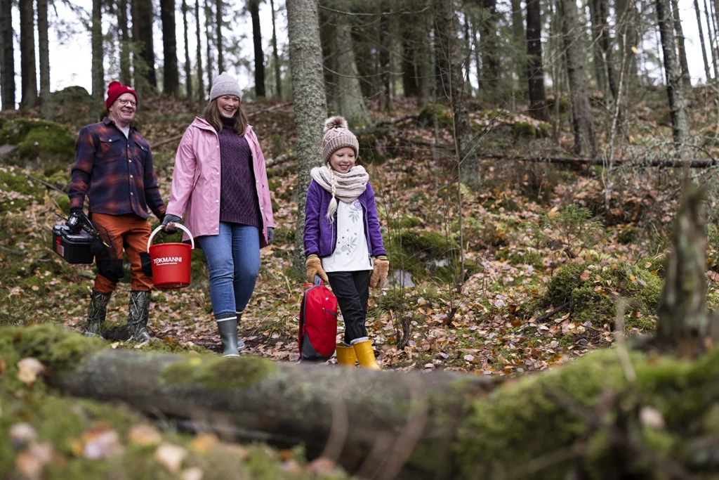 Iloinen kolmihenkinen perhe matkalla kalaan kävellen kuvattuna syksyisessä metsässä.