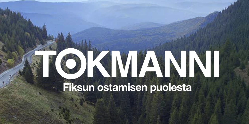 Valkoinen Tokmannin logo valokuvataustalla, jossa näkyy vuoristomaisemaa. Logon alle on keskitetty pienemmän kokoinen teksti: "Fiksun ostamisen puolesta." Logo ja teksti erottuvat hyvin taustasta.