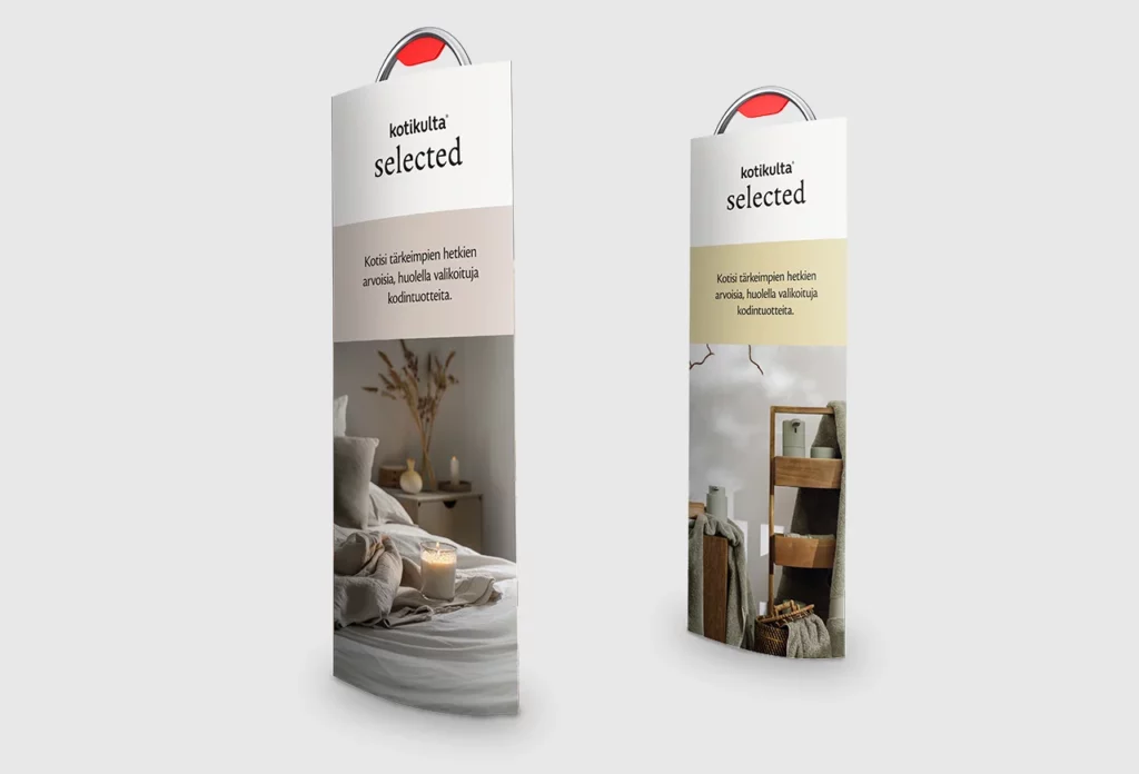 Kaksi Kotikulta Selected -mainostelinettä, joissa yläosassa bränditeksti ja slogan “Kotisi tärkeimpien hetkien arvoisia, huolella valikoituja kodintuotteita.” Vasemman telineen kuvassa pedattu sänky ja palava kynttilä, oikean telineen kuvassa vihreänharmaita pyyhkeitä ja puisia kylpyhuonehyllyjä.
