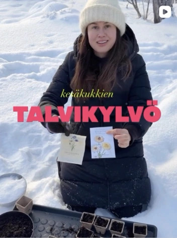 Social media video thumbnail: a woman in a beanie kneeling in the snow with seed packets in her hands, text overlay reads "Winter sowing annuals".
