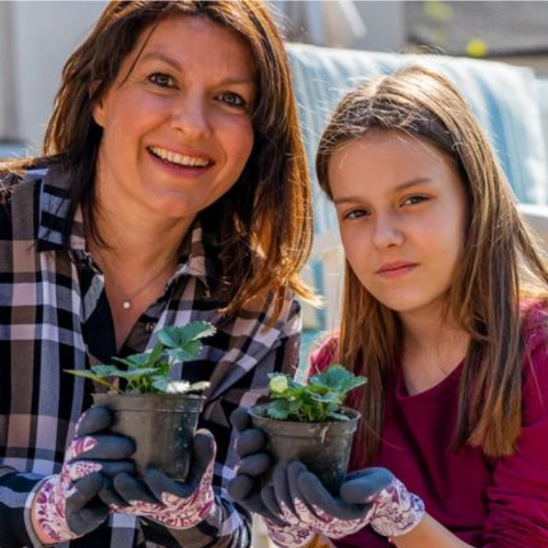Brand persona Linda: a smiling mother in her forties and her young daughter holding seedling pots, wearing gardening gloves.